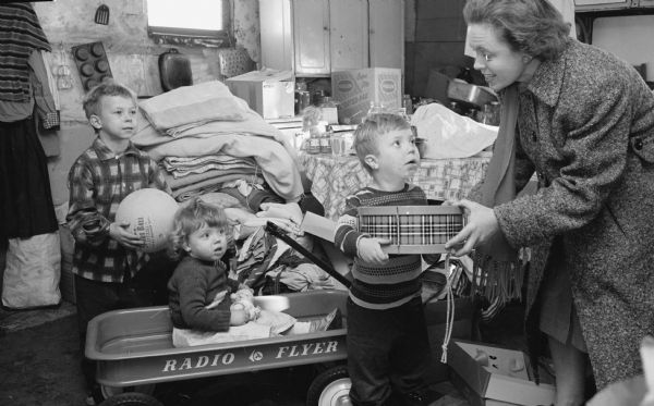 The Empty Stocking Club provides Christmas gifts to the children in the Liggett family of Mazomanie. Shown (L-R) are: Harold (6), Rosie (2) and Alec (3) with Mrs. Wallace Wikoff, Empty Stocking Club Director.  
Mrs. Vernie Leggett was in Madison with the family's baby, Marie (9 months) when the photograph was taken.