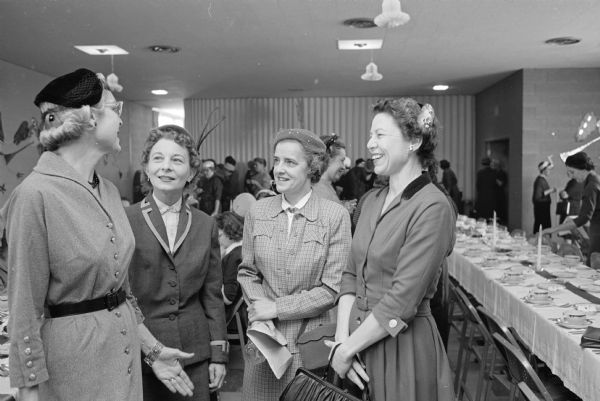 Four women visit during a luncheon given by the Democratic women of Dane county to honor governor-elect Gaylord Nelson's wife, Carrie. Standing are: Alice Ingersoll, Rhea Olmstead, Margaret Watrous, and Julia Miles.