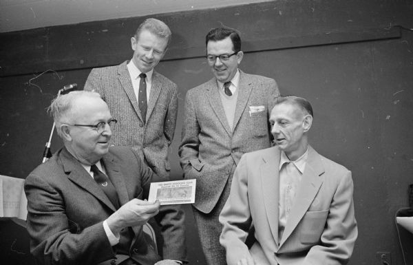 Four men who attended the annual Rounder's Club Christmas party hold an Empty Stocking Club envelope that was used as a place card. Left to right are: Ray H. Schoonover, William Lister, Conrad Lewis, and Robert Hughes.