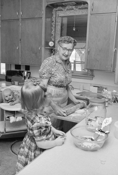 Grandma Bayles rolling out Christmas cookies in the farm kitchen with Ann Denise, 3, and baby Gale, 5 months, nearby. One in a series of images depicting Christmas activities at the 120-acre farm of Mr. and Mrs. Dennis Bayles, Rt 2, Lodi.  