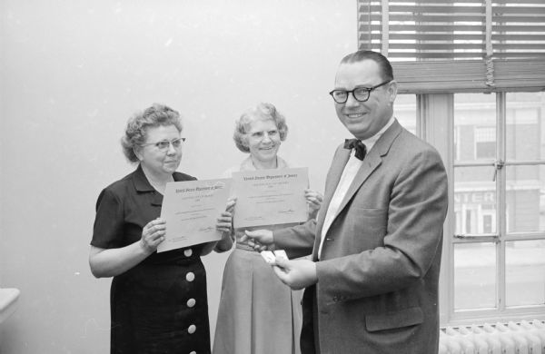 Two women receiving awards for long and meritorious service at the U.S. attorney's office. The women employees are Mrs. Mabel H. Madson, left, Deerfield, who has 15 years, and Mrs. Corinne N. Evans, Madison, who has 20 years. Presenting the women with pins is U.S. Attorney George E. Rapp.