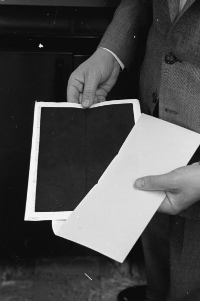 A man is putting an 8 x 10 filter into an envelope to be sent to "a U.S. Public Health Service laboratory in Cincinnati for analysis". The filter changed from white to black after 24 hours exposure to Madison's air.