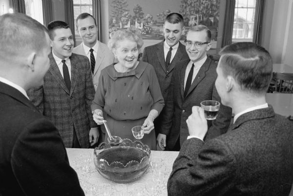 Kappa Sigma fraternity housemother, Mrs. Donald Matheson, serving as hostess with some of  "her boys" in a simulated rushing scene. Included in the picture are: Carl Nelson, Dennis Gehri, Roger Lehman, and John Wendt by her side, and Jerry Seinwill and Peter Korotev in the foreground.