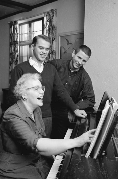 Louise Hackworthy, housemother for the Phi Delta Theta fraternity, playing the piano with two fraternity members, Ralf Torngren and Roger Rumbie.