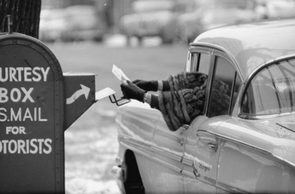 A driver mailing letters into a roadside mailbox from a car at the corner of Monona Avenue and Doty Street. The photograph was taken with a long-lens camera.