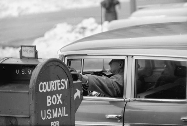 A driver mails a letter in a roadside mailbox from a car on the corner of Monona Avenue and Doty Street. The photograph was taken with a long-lens camera.