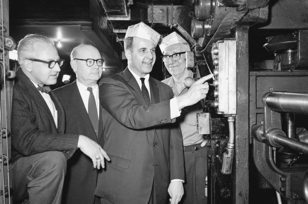 Governor Gaylord Nelson is shown, wearing the traditional pressman's hat, as he pushes the button to start the Wisconsin State Journal press to celebrate the 10th anniversary of the newspaper as a morning paper. Shown (L-R) are: Ray L. Matson, editor; Lawrence H. Fitzpatrick, managing editor; Governor Nelson; and Arthur (Bud) Hillis, night press foreman.
