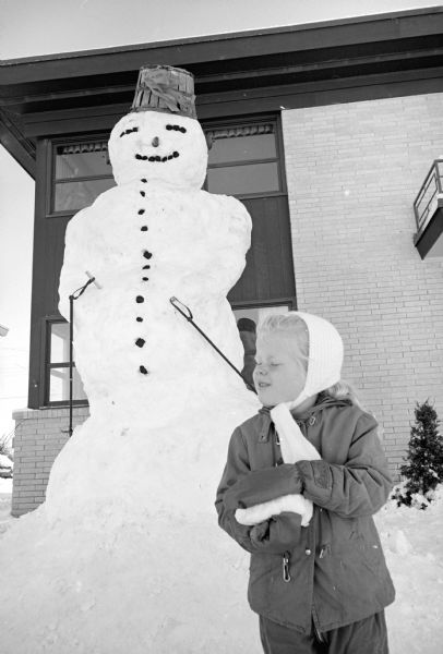 A twelve-foot high snowman is built by Dr. James Messer, Michael Roldt, and Donald Norbert, all living at an apartment building at 505 N. Midvale Boulevard. Kristi Messer (4), daughter of Dr. Messer is shown observing the snowman.