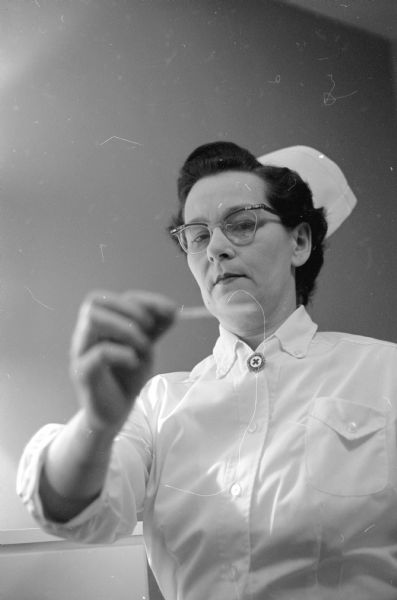 Mrs. Clayton R. Felland, who is a private duty nurse and a mother of two daughters, reading a thermometer.