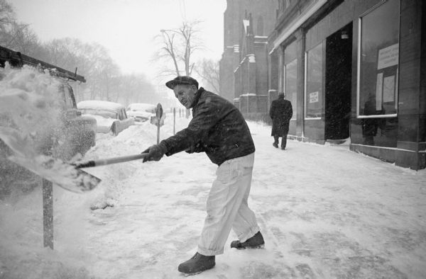 Man shoveling snow on the sidewalk of North Carroll Street. Grace Episcopal Church is visible in the background.