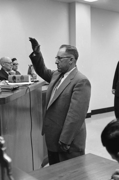 The Madison Police and Fire Commission explores a traffic accident involving Police Chief Bruce Weatherly and witnesses' claims that he was under the influence of liquor the evening of the accident.<br>Truck driver Norman Parmenter, involved in the January 8, 1959 crash with Police Chief Weatherly's squad car, takes the oath to testify before the commission.</br>