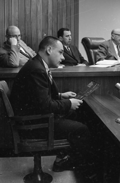 The Madison Police and Fire Commission explores a traffic accident involving Police Chief Bruce Weatherly and witnesses' claims that he was under the influence of liquor the evening of the accident.<br>William H. Best, former Blooming Grove policeman, describes the January 8, 1959 accident scene to the commission. Shown in background (L-R) are commission members Thomas Doran; James E. Doyle; and Albert Toubert, commission chairman.</br>