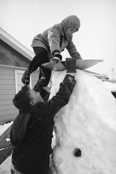 Howard Schwartz (13) helps his brother Larry (9) climb aboard a flying saucer on top of the snow slide they built in their front yard at 4322 Wakefield Street.