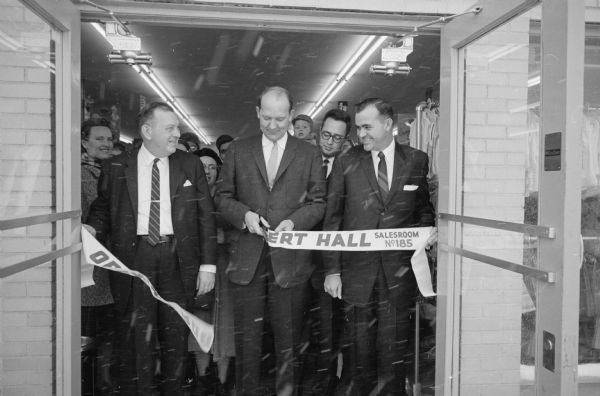 Mayor Ivan Nestingen is shown cutting the ribbon to officially open the reconstructed Robert Hall salesroom, 3205 E. Washington Avenue after the interior was destroyed by fire January 16. Looking on are Edward Cline, manager (left) and John Horn, district manager from Milwaukee. Standing behind is William Small, assistant manager.