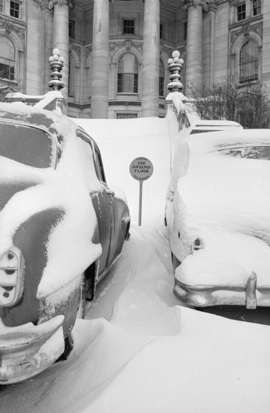 Snow covered steps of the capitol building, as well as two cars covered with snow. Sign between the cars reads: "Use Ground Floor". The caption adds: "Well, What Else?"