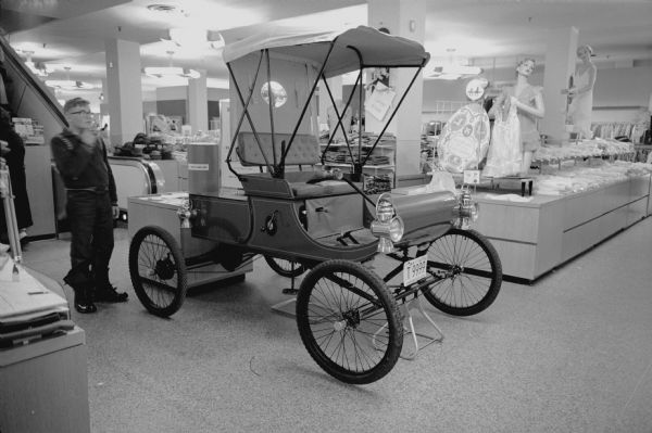 A reproduction of a 1901 Oldsmobile at Pyramid Motor Company, 434 West Gilman Street. It is owned by Sears Roebuck and Company and is part of an open house sponsored by the Madison Automobile Association.