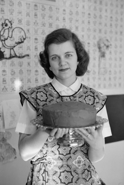 When Joan Carlton of Oakpark, Illinois married Reed Forbush of Appleton, Wisconsin she was skeptical of life as a minister's wife. Now, as a series of photographs shows, she enjoys her life as the wife of the pastor of Middleton Community church. Joan is holding a cake in her hands.