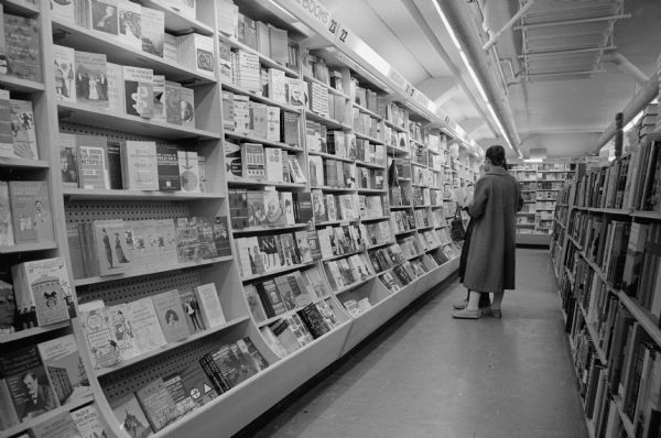 An aisle of paperback books in a Madison bookstore. Two women are standing in the aisle.
