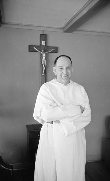 Portrait of the Very Rev. Geary, standing in front of a crucifix. He will be the new pastor of Blessed Sacrament Catholic Church, 2181 Rowley Avenue.