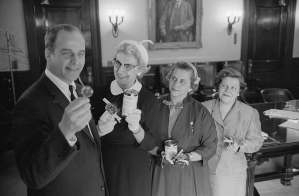 Wisconsin Governor Gaylord Nelson receives a poppy in his office from Selma Mepham, chairman of the 1959 state poppy drive. Looking on are Florence Woolever and Kay Brahm, both members of American Legion auxiliaries. Proceeds from the sale of poppies are used to help disabled and needy veterans.
