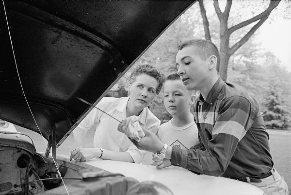 Mrs. Jean Wirka is being shown how to check oil in her car by her son, John, 14. Her other son, Eddie, 11, is watching the process.