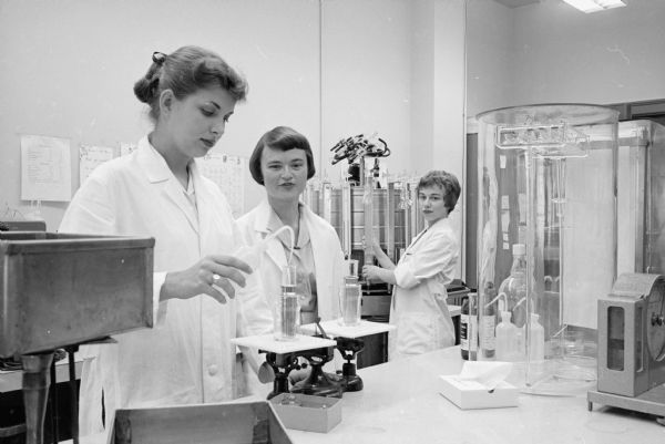 Working with two West High students in a chemical research laboratory of the U. W. Medical School, is Dr. Anna Maria Williams, center. At left, Mary Sedgwick, performs a lab test and at right Marjorie Kowitz works on an apparatus. They are participants in a program in which members of Madison's Beta chapter of Sigma Delta Epsilon, an international organization for women doing independent scientific research, work with a group of high school girls chosen for their outstanding aptitude and interest in science.