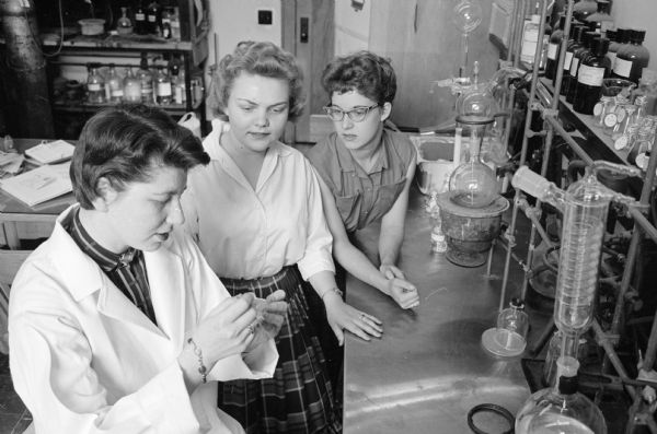 Demonstrating a research procedure to high school female students at a U.W. chemistry research laboratory is Dr. Carolyn Abrahams, left.  Barbara Swanson, center and Linda McDaniels are looking on. They are participants in a program in which members of Madison's Beta chapter of Sigma Delta Epsilon, an international organization for women doing independent scientific research, work with a group of high school girls chosen for their outstanding aptitude and interest in science.