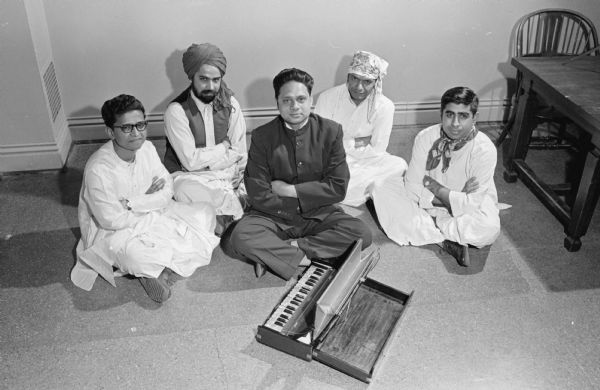 Five unidentified University of Wisconsin students, all sitting cross-legged on the floor with a small portable pump organ or harmonium. In South Asia, the harmonium is a common accompaniment for vocal music, so this may be a musical group.