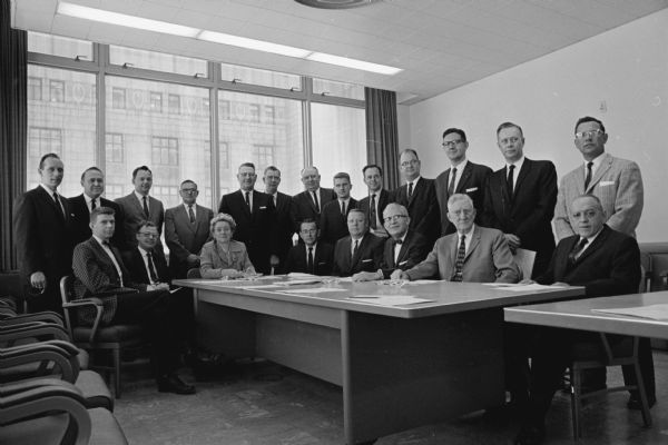 The 1960 Madison City Council poses for a group portrait in the City County Building. The State Office Building at 1 West Wilson Street can be seen through the large windows.
