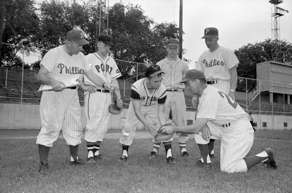 Kneeling at right is baseball scout, Emil Belich, showing Bill Hebl, Sun Prairie, how a catcher should scoop a ball during a session of the Phillies' baseball school at Breese Stevens field. Looking on are, left to right: Eddie Dancisak, Phillies supervisor of Midwest scouting; Dan Weiskopf, Sheboygan; Ken Grauvogl, Madison; and Bill Freese, Phillies scout.