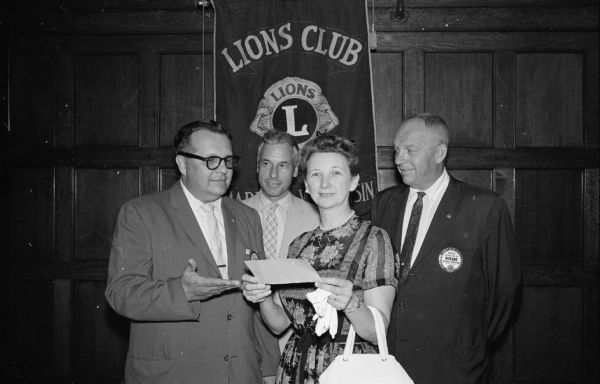 Donald Franklin, left, presenting a check for $400 to Mona Manson, as the club's contribution toward improving Camp Maria Olbrich, the YWCA day camp on Lake Mendota. Looking on are Julian Clark, Waunakee, and Harlow Rickard, right.
