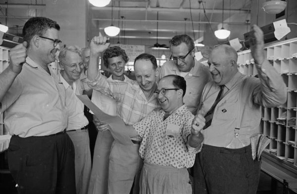 A group of six smiling postal workers are listening as Floyd Switzky, center, reads the news that Congress voted to override President Eisenhower's veto of an act to provide pay raises for 1.5 million federal workers.