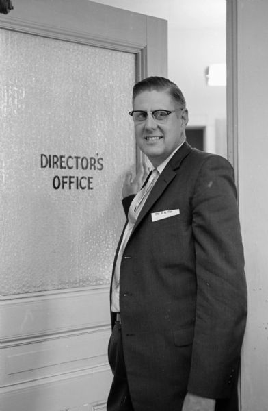Norman Mitby, the new director of the Madison Vocational and Adult school, standing next to a door marked "Directors Office."