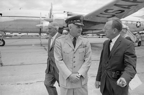 General Nathan F. Twining, Chairman of the Joint Chiefs of Staff (1957-1960), arrives at Truax Field on his way to visit his hometown of Monroe on the 4th of July holiday. General Twining is shown visiting with Edmund C. Hamilton (R), editor of the <i>Monroe Evening Times</i>. George Van Wagenen, a friend of General Twining, is shown in the background.
