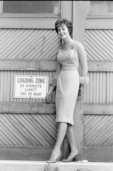 A model poses by loading dock doors. Sue Reynoldson wears a beige cocktail dress that's cuffed in lynx. Miss Reynoldson attends Rollins College, Winter Park, Fla. where she will be a sophomore.