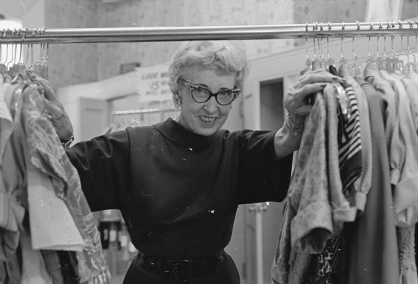 Mrs. Lou Nelson is shown framed by a rack of clothing at her business, Olson's, Inc., a women's apparel store at 105 State Street. She is a grandmother of three, works six days a week, is a partner in the business with her only son, John B. Nelson. She enjoys making several buying trips to New York City and Chicago each year.
