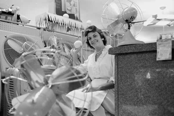 An unknown woman sits in front of several electric fans on a hot summer day.