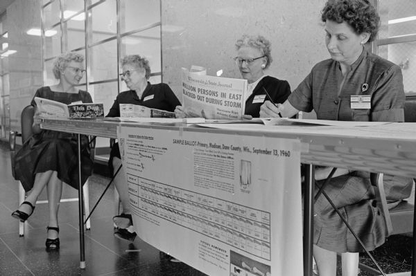 Poll workers pass the time during a light turnout for the 1960 primary in the 1st precinct of the Third Ward held at the City-County Building. Shown (L-R) are: Mrs Mabel Burrington, 518 S. Paterson Street, and Mrs. Zella Bender, 143 S. Hancock Street, reading magazines; Mrs. Beulah Reeth, 309 Spaight Steet, reading a copy of the morning newspaper; and Mrs. Mabel Pope, 518 Paterson Street, catching up on letter writing.  