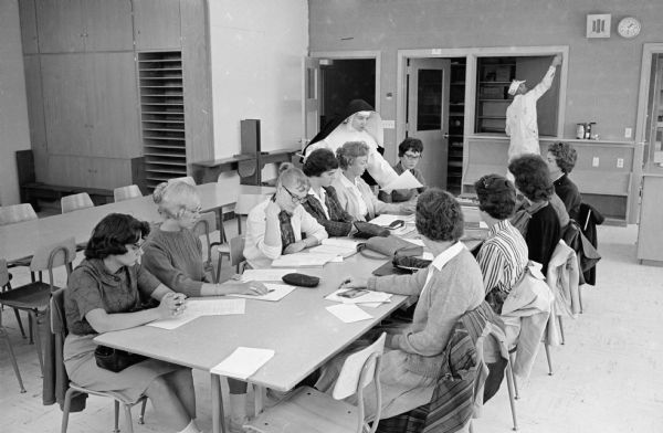 A painter puts on the finishing touches in a classroom in the new De Ricci Hall building on the Edgewood College campus, 855 Woodrow Street, as Sister M. Terrestra, O. P., distributes papers to her students.
The new $750,000 building contains 24 classrooms and administrative offices and is named for the Dominican Saint Catherine De Ricci.