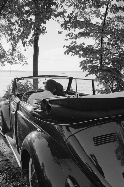 A couple sitting in their VW Beetle convertible car look out over a Madison lake on a nice September day.