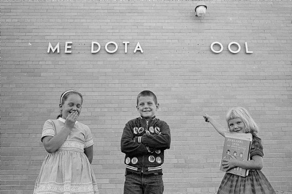 Three children are amused by the incomplete sign on the new Mendota Elementary School, 4002 School Road. Shown (L-R) are Debbie Uselmann, second grade; John Greiert, third grade; and Lori Hoffman, first grade.