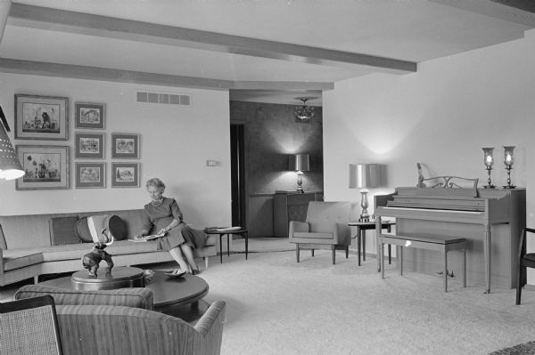 Mrs. Velma "Pem" Wheaton, Milwaukee, who designed the interior of the Arthur O. Schroeder home, sits beneath a picture grouping that carries out the room's color accents.