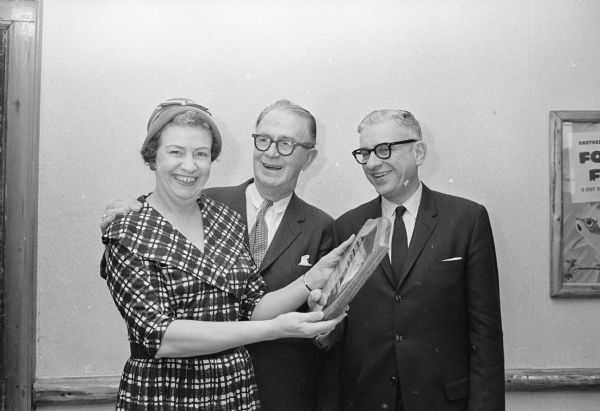 A Roundy's Fun Fund plaque is presented to Mrs. Leia Josephson (L), 225 Van Deusen Street by Joseph (Roundy) Couglin (Middle), Wisconsin State Journal columnist and founder of the fund for handicapped and underprivileged children, and Walter Frautschi, president of the Democrat Printing Company. The plaque is in honor of Mrs. Josephson's many years of volunteer service in supervising the mailing of appeal letters and keeping contribution records for the fund. The Democrat Printing Committee was honored for helping keep printing costs for the fund down by allowing its' letter shop to process portions of the work on off seasons. Mrs. Josephson is manager of the Democrat Printing Company letter shop.
