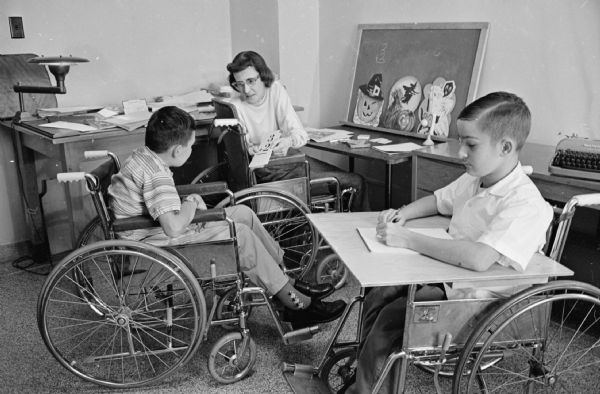 A scene at the Wisconsin Neurological Foundation, 1954 East Washington Avenue, which is observing it's 10th anniversary.  Multiple sclerosis patient Loretta Leverance, a former teacher, is teaching two boys in wheelchairs in a part of her room which she converted into a classroom.    The pupils are Boone West, Stockbridge, Michigan and Olen Gilley, Premium, Kentucky.    