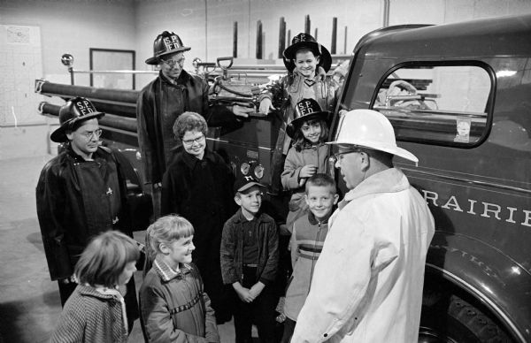 Members of Diane Schmitt's Sun Prairie school's third grade are greeted by Volunteer Fire Department chief Ben Blaschka during a tour of the fire station. Students are Donna Clark, Priscilla Laper, Dale Burke, Dennis Pederson, Janet Frye, and Eddie Savering. Two firemen in the background are George Straus and EmdenjSchey.