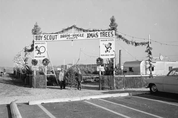 Madison Boy Scout Drum and Bugle Corps representatives receive a shipment of Christmas trees to sell at their two tree lots at the 1200 block of East Washington Avenue and the Midvale Plaza in the 500 block of S. Midvale Boulevard to raise funds to finance activities during the next year. Shown are, (L-R) C. H. Beebe, executive director of the corps; Oscar Dary, a member of the corps; and Raymond Houtler, assistant drumming instructor. (from the caption in The Capital Times, December 8, 1960, photo.)
