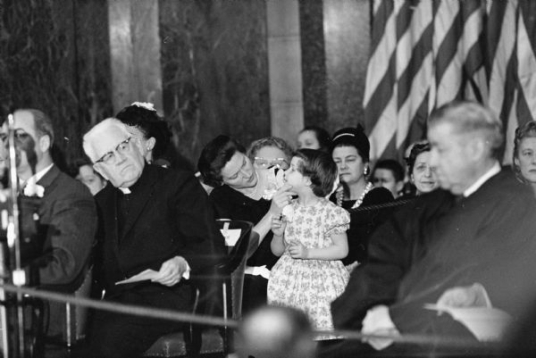 Cynthia (Tia) Nelson, age 4, wanting a little attention from her mother, Mrs. Gaylord Nelson just before Governor Gaylord Nelson takes his oath of office in the State Capitol. At the left is Bishop William P. O'Connor of the Catholic Diocese of Madison.