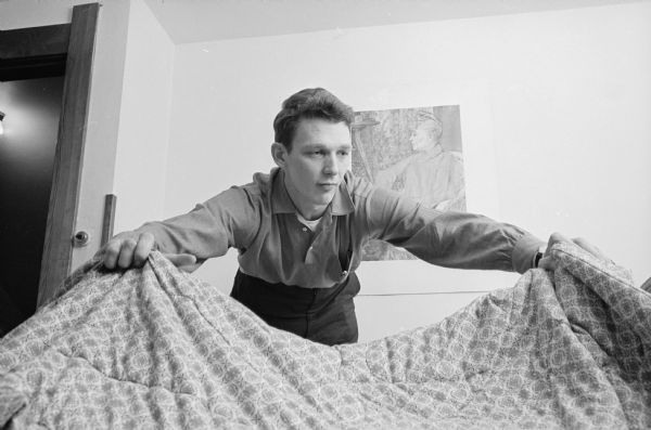 One in a series of photographs of four U.W. physics graduate students who are renting a furnished home at 429 Russell Walk. In this photograph Brandt Kehoe is shown making his bed.