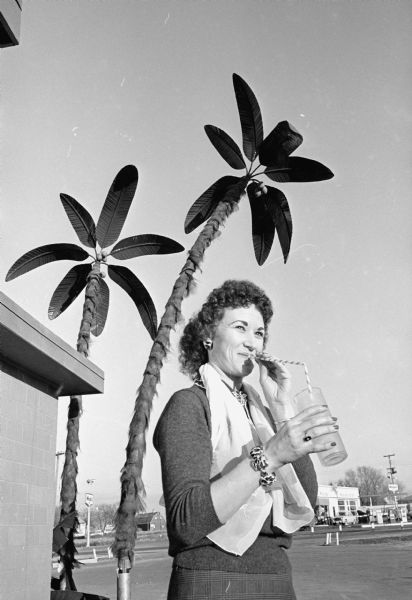 Mrs. Dorothy Brewer poses next to artificial palm trees that are part of a remodeling project of the Red Rooster restaurant on East Washington avenue, which will reopen as the Golden Rooster. The managers are Romie Schneider and Bernie Matney.