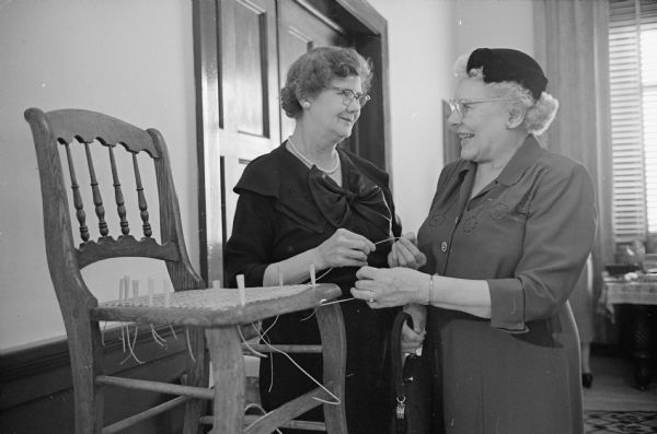 Amelia Flemming demonstrates her chair caning to Edna Lundy at the hobbies and craft show of the Woman's Club of Madison.